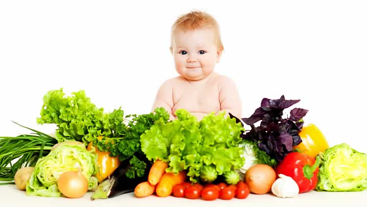 Годовалый малыш сидит рядом с большой горой овощей и зелени