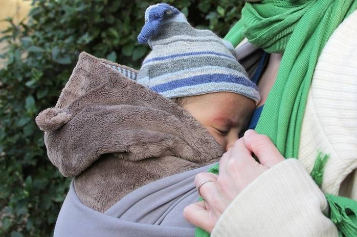 Ребенок на руках у мамы в сером костюмчике и шапочке на прогулке